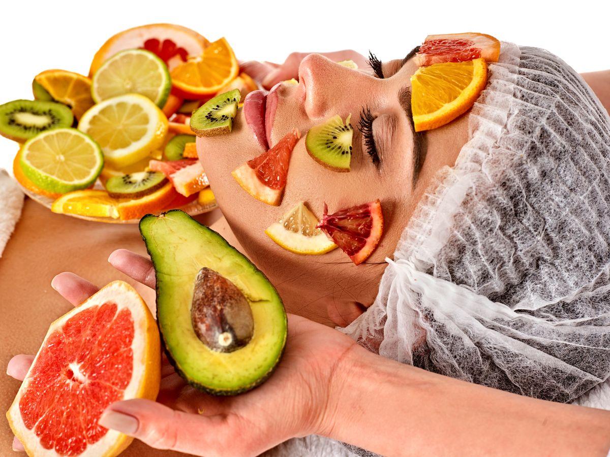 Genesis Vegan Spa mask from fresh fruits for woman. Beautician apply slices of avocado, grapefruit and kiwi. Treatment of warts with fruit masks. Female enjoys procedure. Top view.